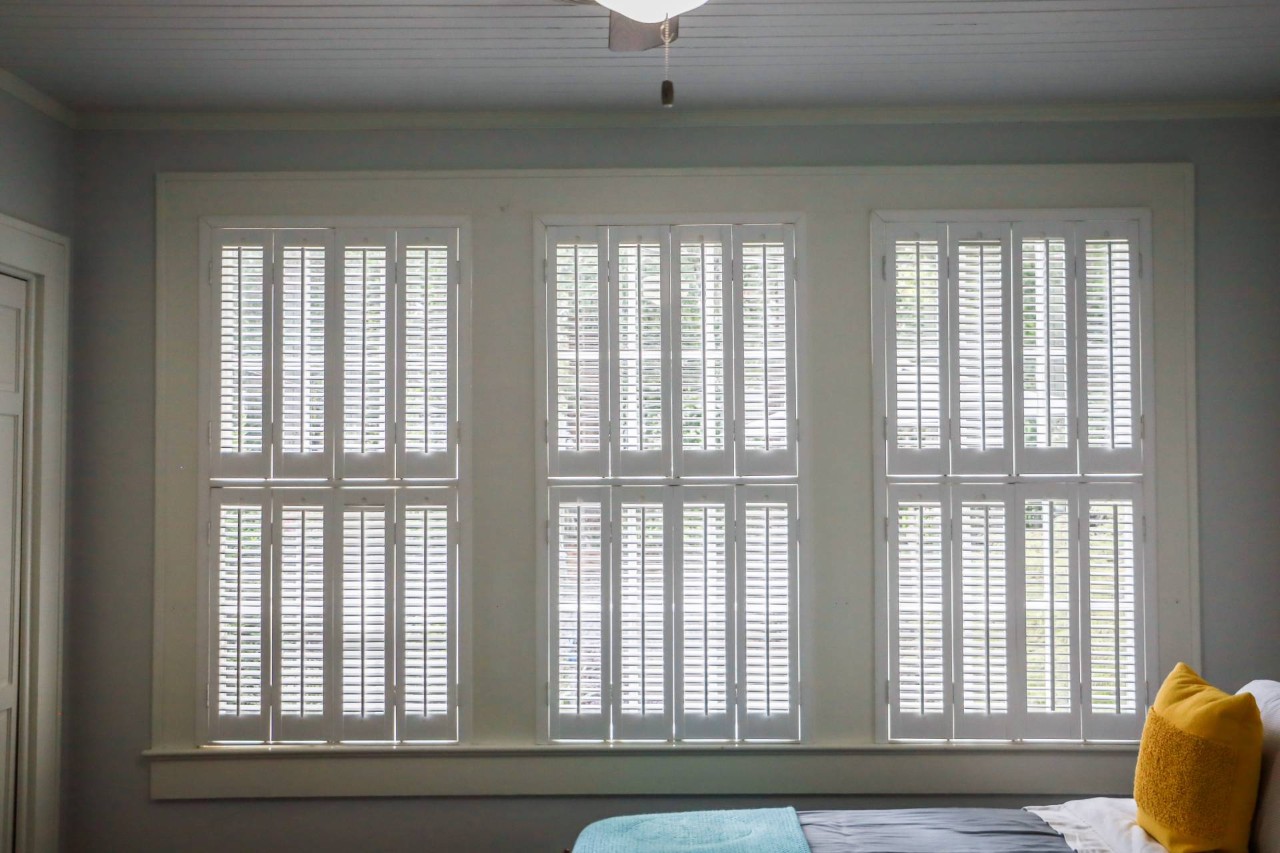 Three large windows with cream-colored plantation shutters in a bedroom at Blinds Plus near Springfield, Missouri (MO) 