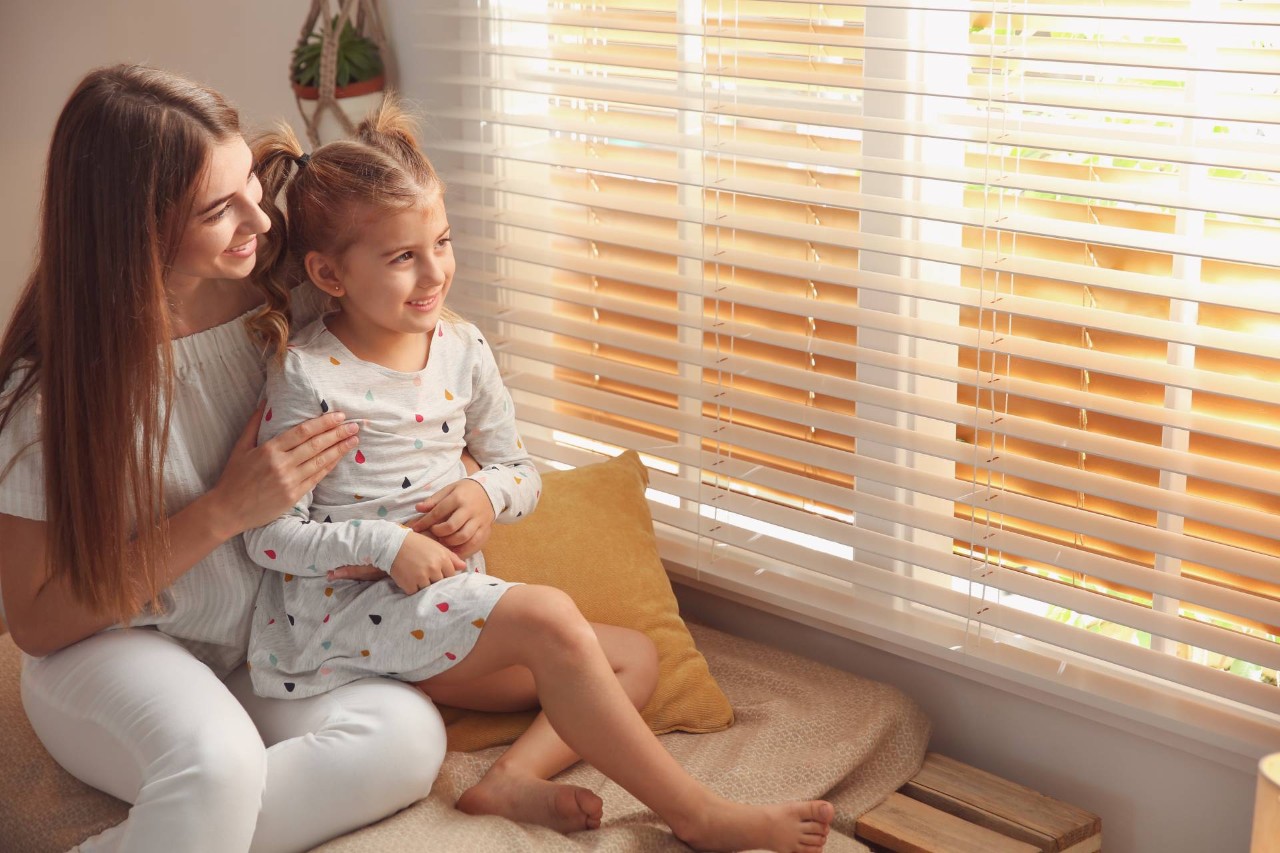 Two people sitting by a well-lit window with horizontal blinds at Blinds Plus near Springfield, Missouri (MO)